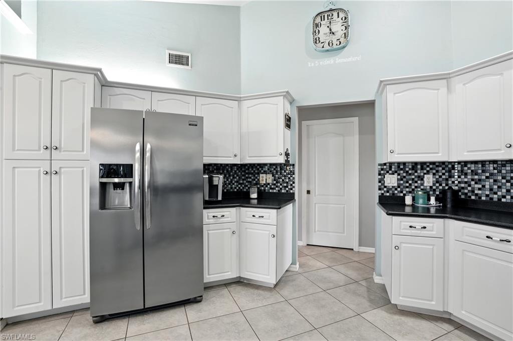 Kitchen with stainless steel refrigerator with ice dispenser, dark countertops, a towering ceiling, light tile patterned floors, and white cabinetry