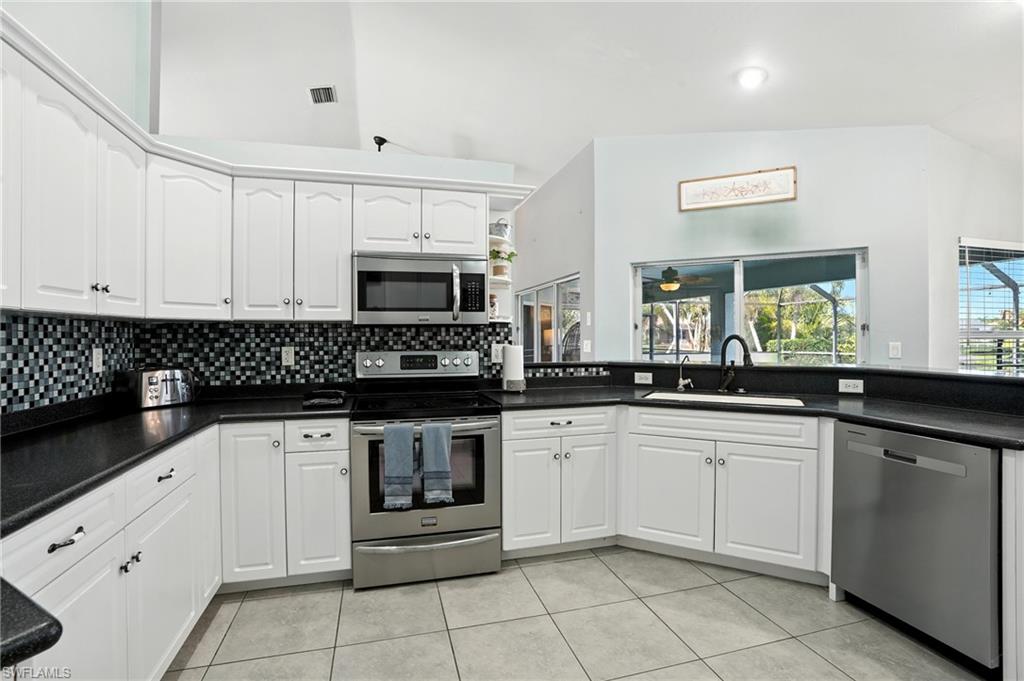 Kitchen with appliances with stainless steel finishes, lofted ceiling, tasteful backsplash, light tile patterned flooring, and white cabinetry