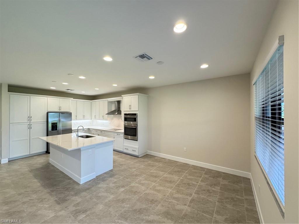Kitchen featuring white cabinetry, a kitchen island with sink, recessed lighting, fridge, and range hood