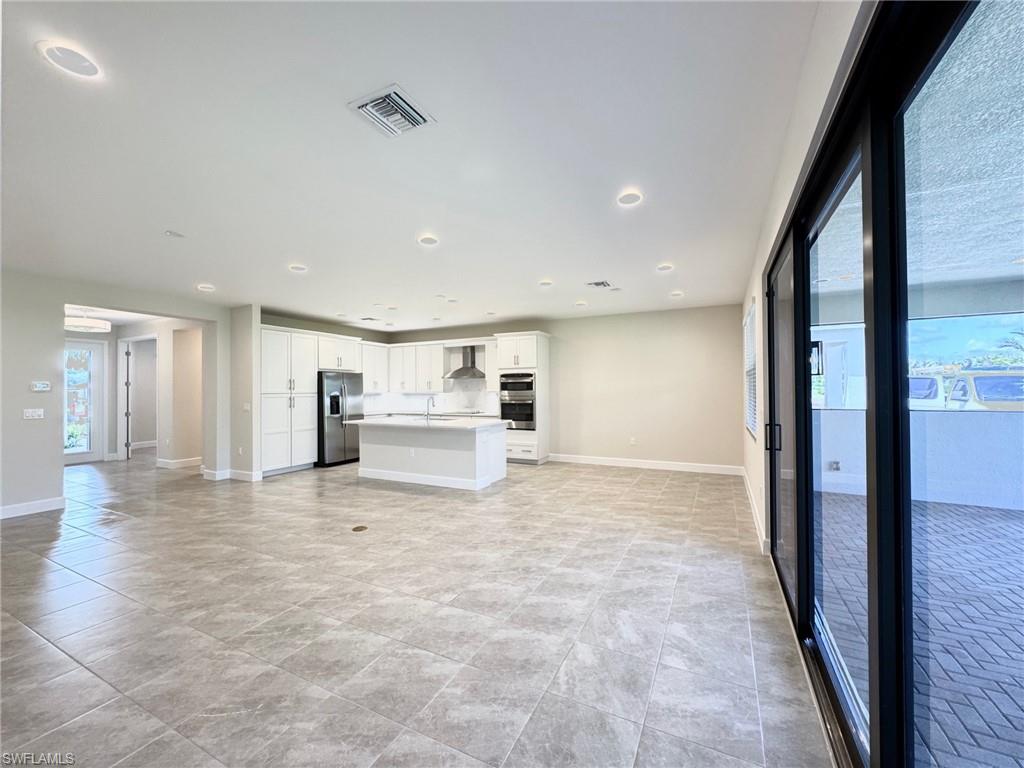 Kitchen featuring white cabinets, stainless steel appliances, light countertops, a kitchen island with sink, and open floor plan