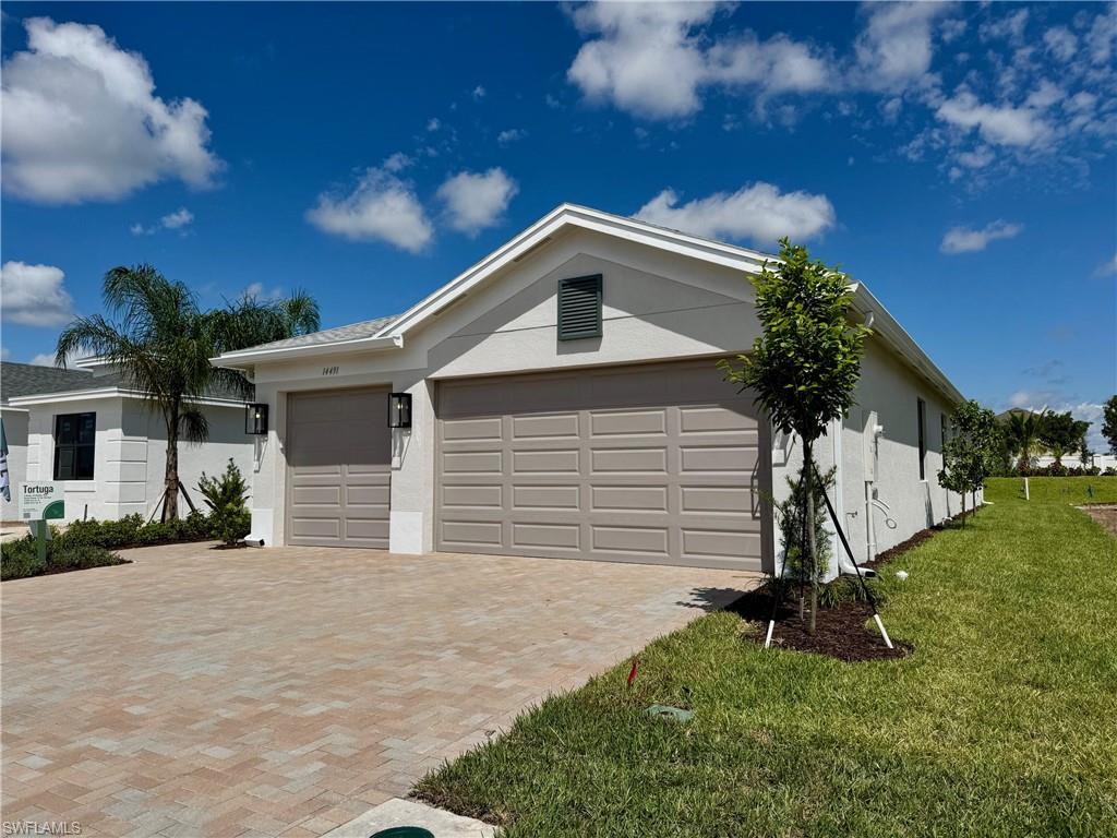 View of front of property with stucco siding, decorative driveway, an attached garage, and a front yard