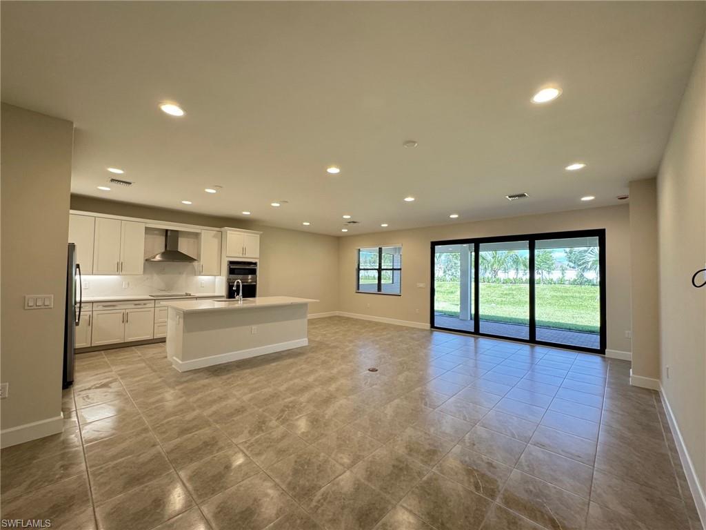 Kitchen with white cabinetry, an island with sink, recessed lighting, decorative backsplash, and wall chimney range hood