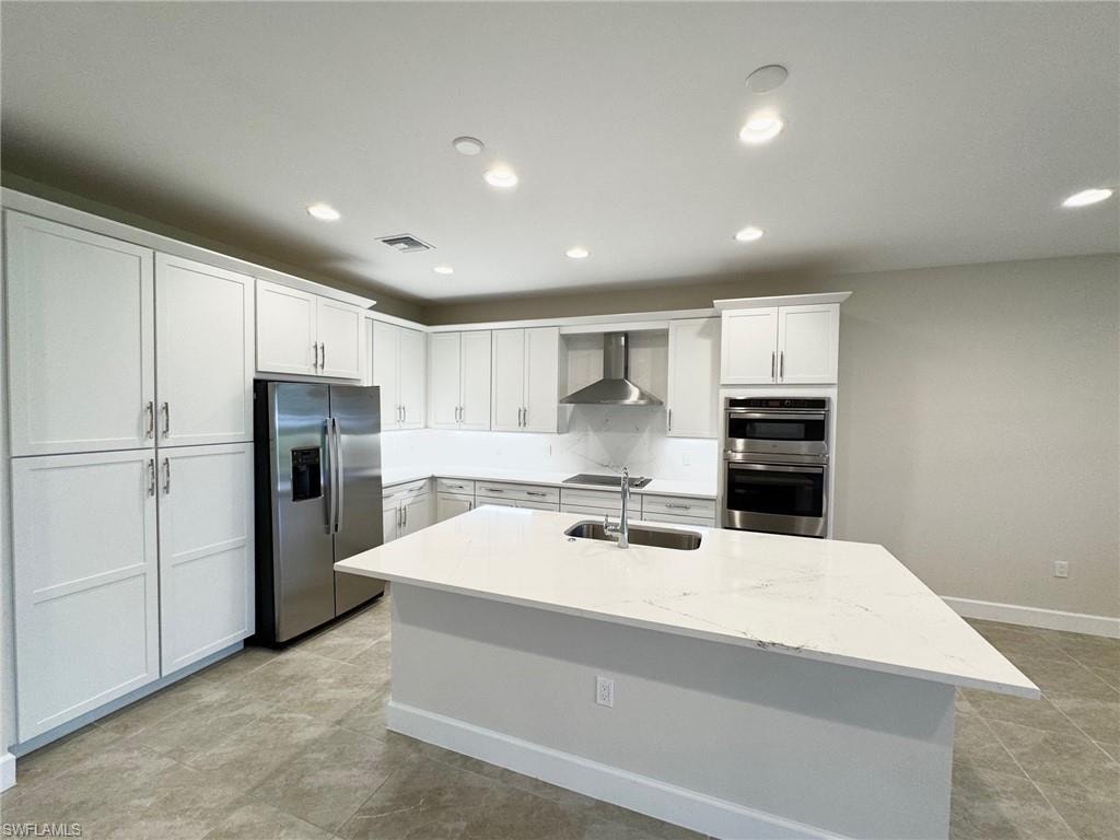 Kitchen featuring light stone countertops, white cabinetry, appliances with stainless steel finishes, recessed lighting, and wall chimney exhaust hood