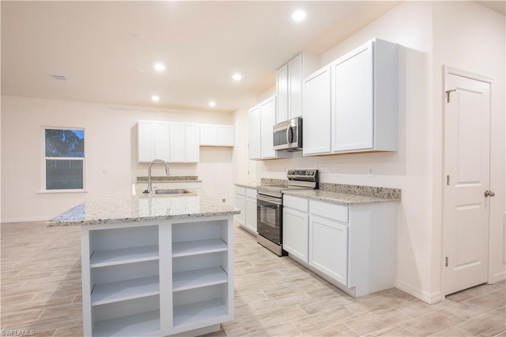 Kitchen with open shelves, stainless steel appliances, light stone countertops, wood finish floors, and recessed lighting