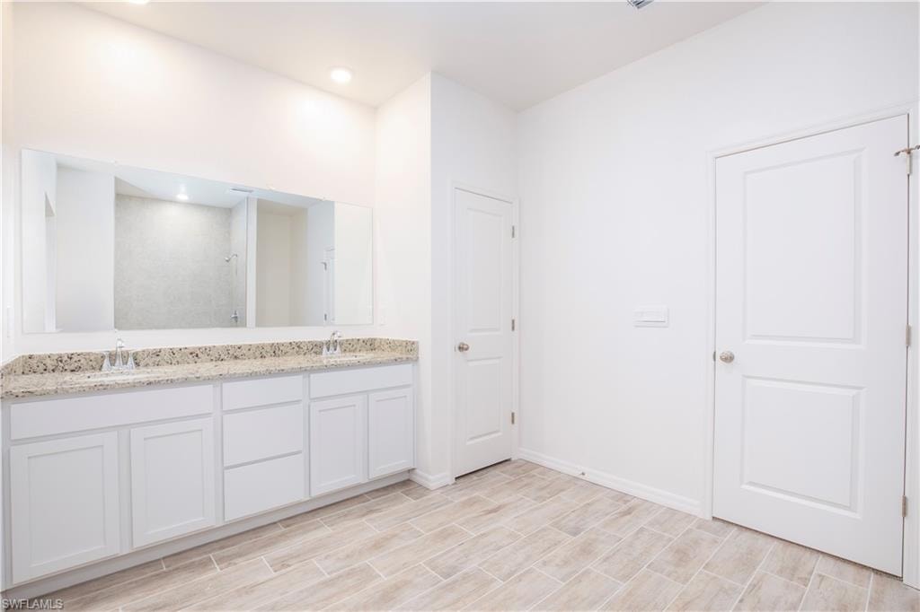 Full bathroom with double vanity, a walk in shower, and wood finish floors