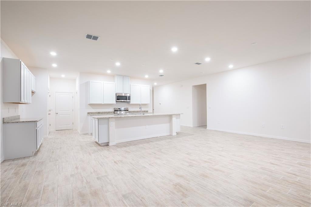 Kitchen with white cabinets, light wood-style flooring, stainless steel appliances, a kitchen island with sink, and recessed lighting