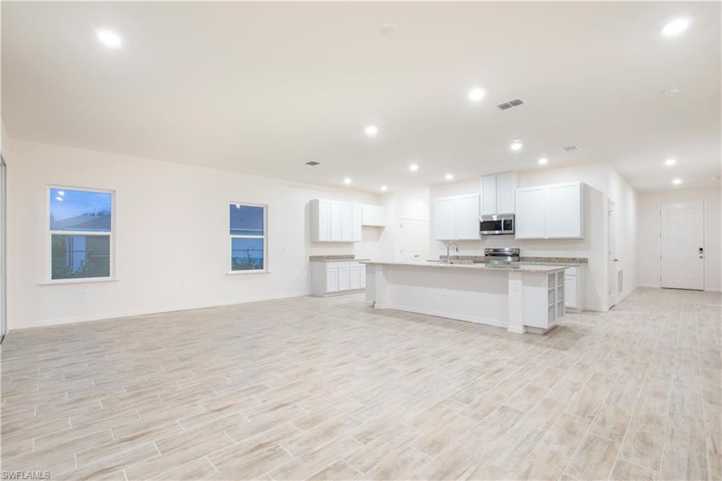 Kitchen featuring a kitchen island with sink, wood tiled floors, white cabinets, open floor plan, and recessed lighting