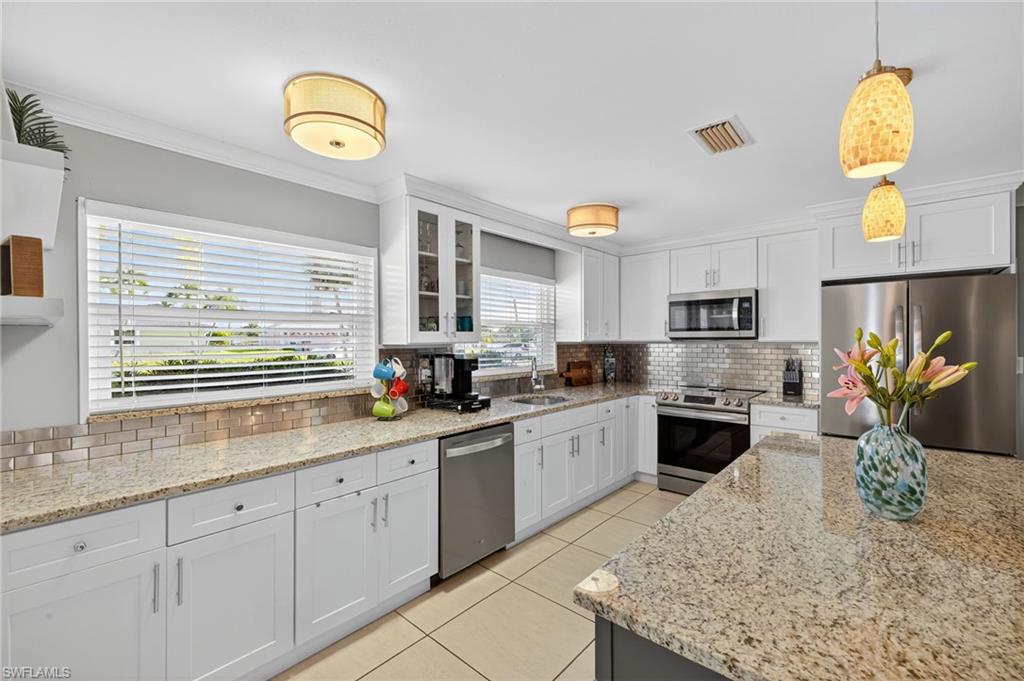 Kitchen with white cabinetry, backsplash, stainless steel appliances, decorative light fixtures, and light tile patterned floors