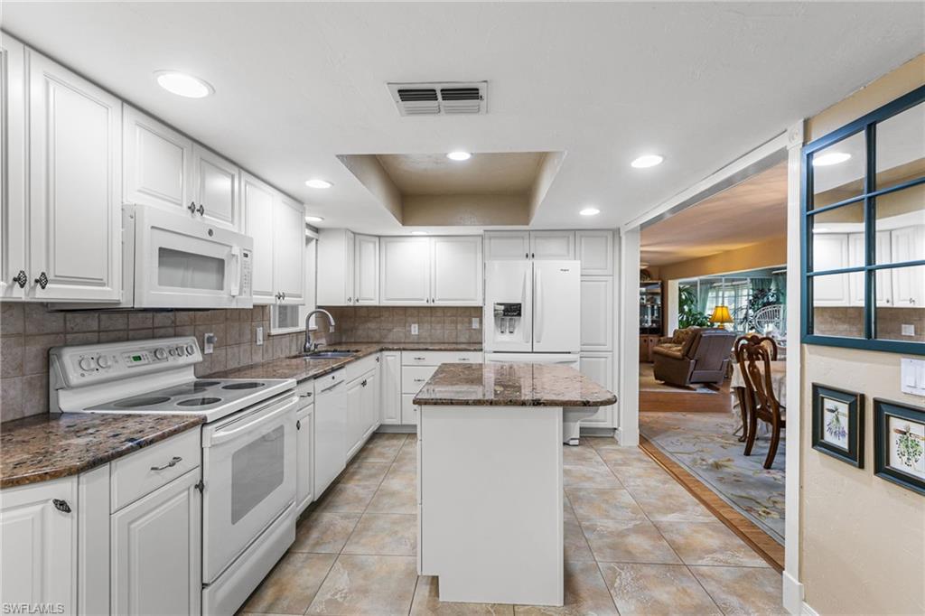Kitchen featuring white appliances, dark stone countertops, white cabinets, a center island, and recessed lighting