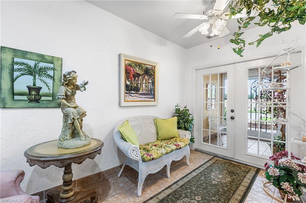 Under-air entry way styled as a Sitting room with french doors, a textured wall, and ceiling fan