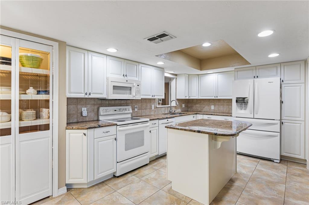 Kitchen with white appliances, decorative backsplash, dark stone countertops, white cabinets, and recessed lighting