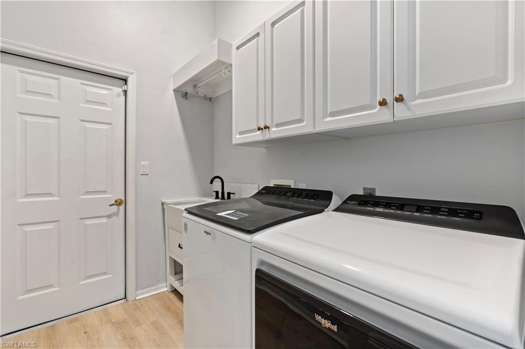 Washroom with light wood-style flooring, cabinet space, and washing machine and clothes dryer