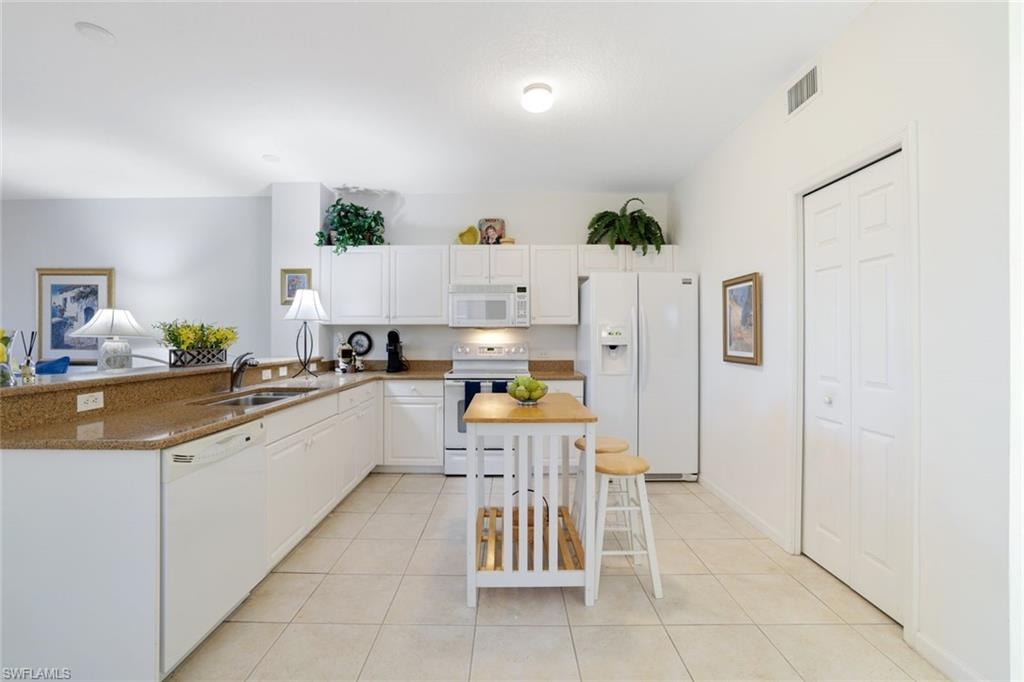Kitchen with white appliances, white cabinets, light tile patterned flooring, and dark stone countertops