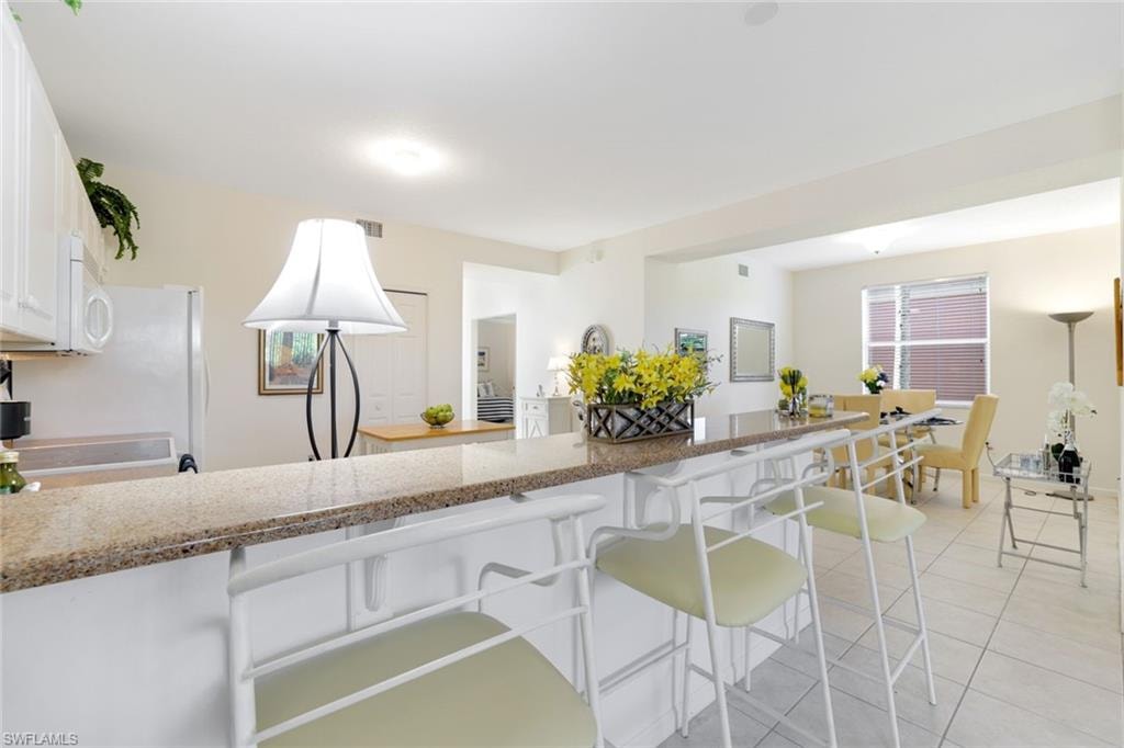 Kitchen featuring white cabinetry, light stone countertops, light tile patterned floors, a peninsula, and a kitchen bar