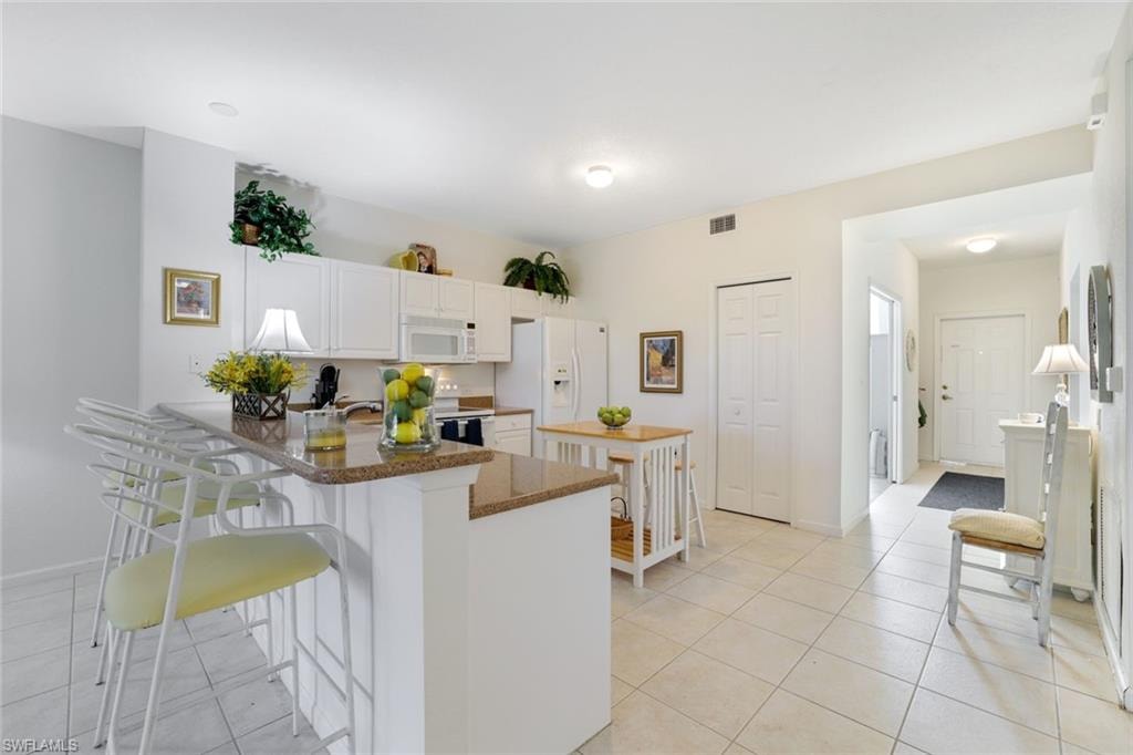 Kitchen with white cabinets, light tile patterned flooring, a breakfast bar area, and white appliances
