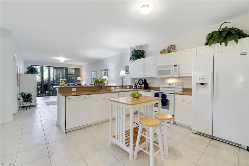 Kitchen featuring white appliances, white cabinetry, a peninsula, light tile patterned floors, and expansive windows
