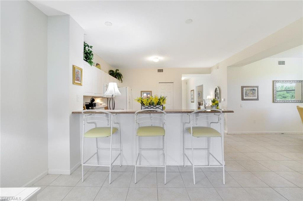 Kitchen featuring a peninsula, white cabinetry, a kitchen bar, light tile patterned floors, and dark stone countertops