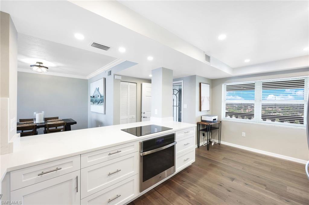 Kitchen featuring stainless steel oven, black electric cooktop, white cabinetry, hardwood / wood-style flooring, and ornamental molding