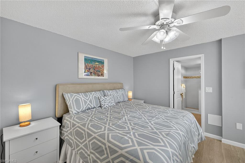 Bedroom featuring ensuite bathroom, light wood-style floors, a textured ceiling, and a ceiling fan