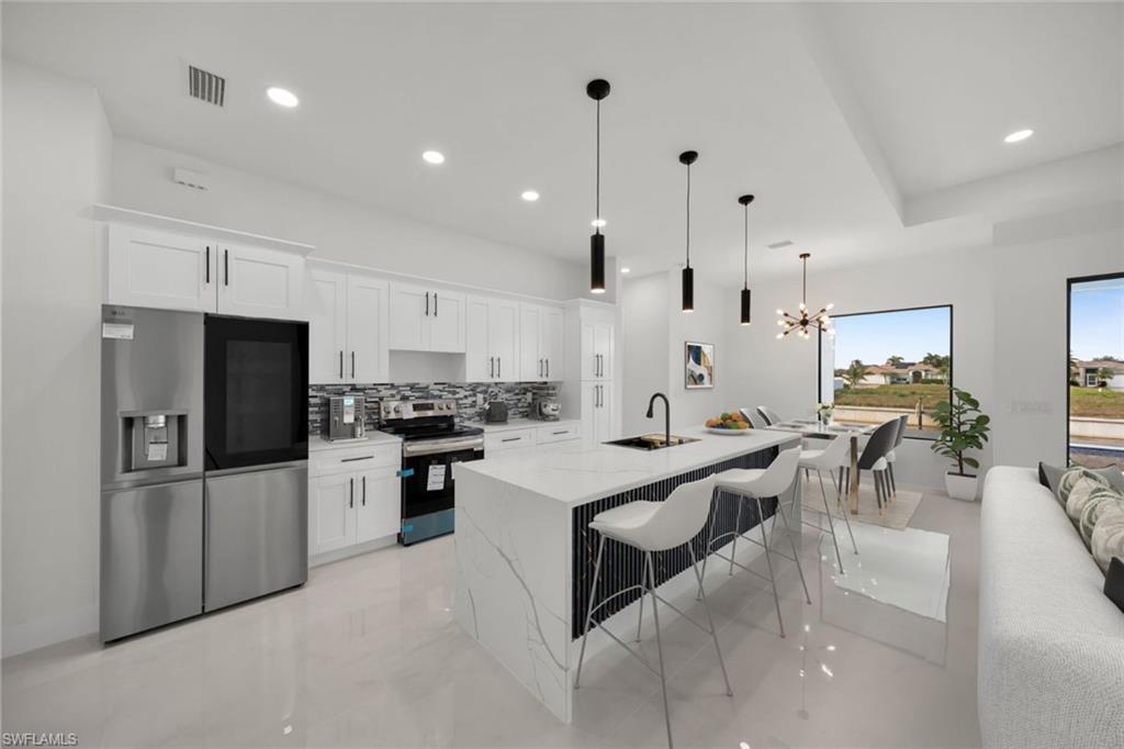 Kitchen featuring decorative light fixtures, light stone countertops, recessed lighting, white cabinetry, and an island with sink