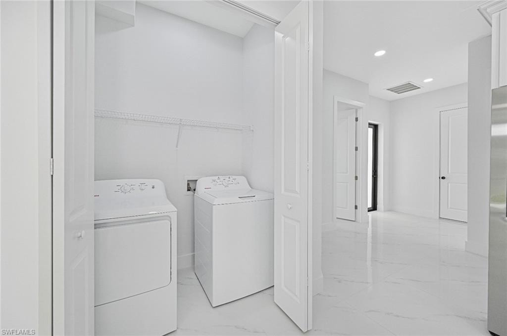 Laundry room featuring light marble finish flooring, independent washer and dryer, and recessed lighting