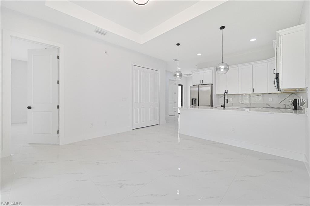 Unfurnished living room featuring light marble finish flooring, recessed lighting, and a tray ceiling