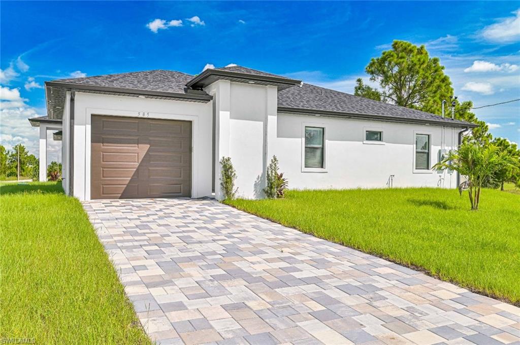 Prairie-style home with decorative driveway, a garage, a front lawn, stucco siding, and a shingled roof