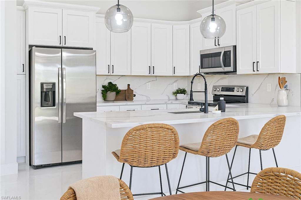 Kitchen with appliances with stainless steel finishes, a breakfast bar, white cabinets, and tasteful backsplash