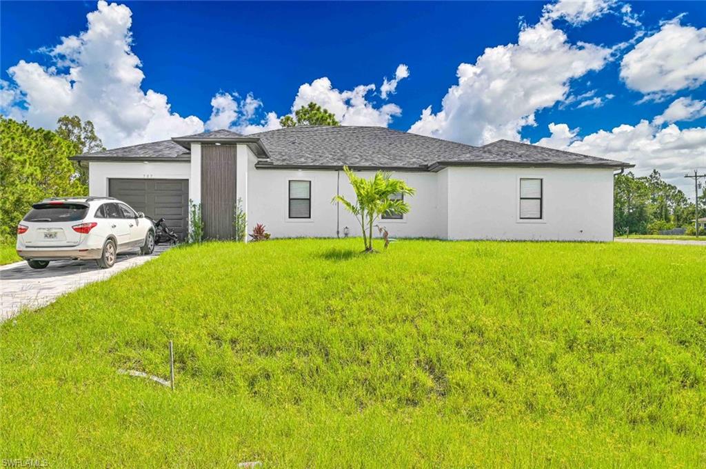 View of front of property with an attached garage, stucco siding, driveway, a front lawn, and roof with shingles