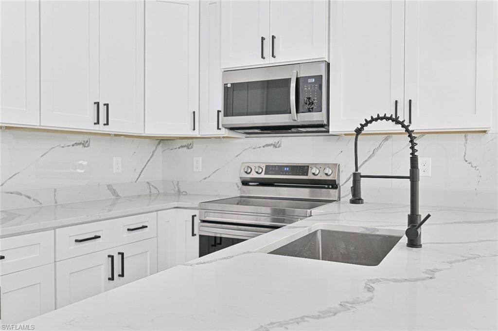Kitchen with white cabinetry, tasteful backsplash, light stone countertops, and stainless steel appliances
