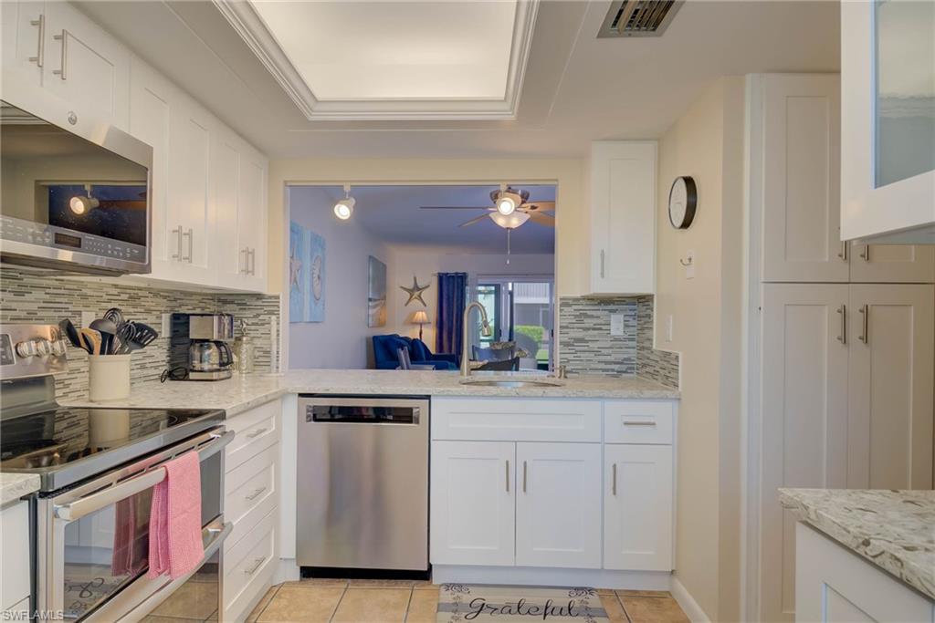 Kitchen featuring stainless steel appliances, white cabinetry, light tile patterned floors, and backsplash