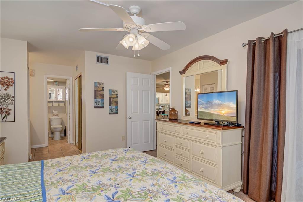 Bedroom with light tile patterned floors, ceiling fan, and ensuite bathroom
