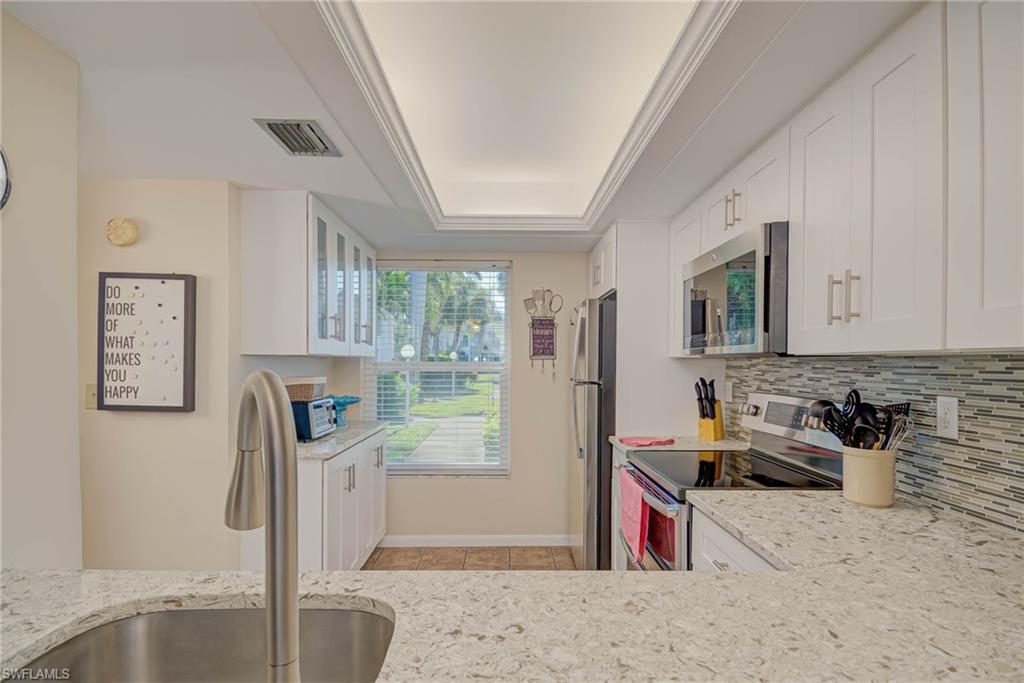Kitchen with white cabinetry, stainless steel appliances, light stone counters, a tray ceiling, and decorative backsplash