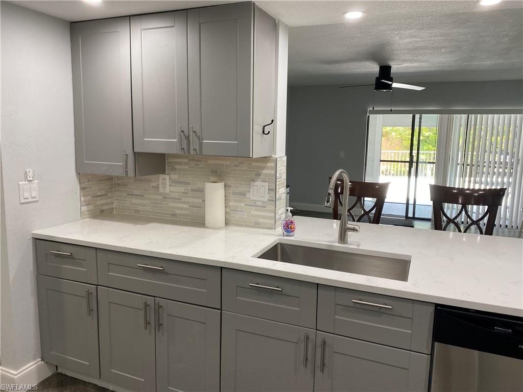 Kitchen featuring gray cabinets, light stone counters, backsplash, recessed lighting, and a textured ceiling