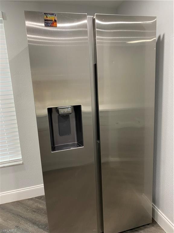 Kitchen view of a textured wall, stainless steel refrigerator with ice dispenser, and dark wood finished floors