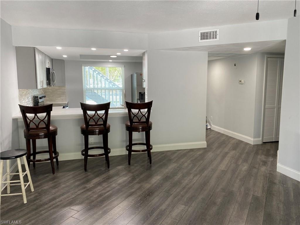 Kitchen with light countertops, dark wood-style flooring, a kitchen breakfast bar, recessed lighting, and decorative backsplash