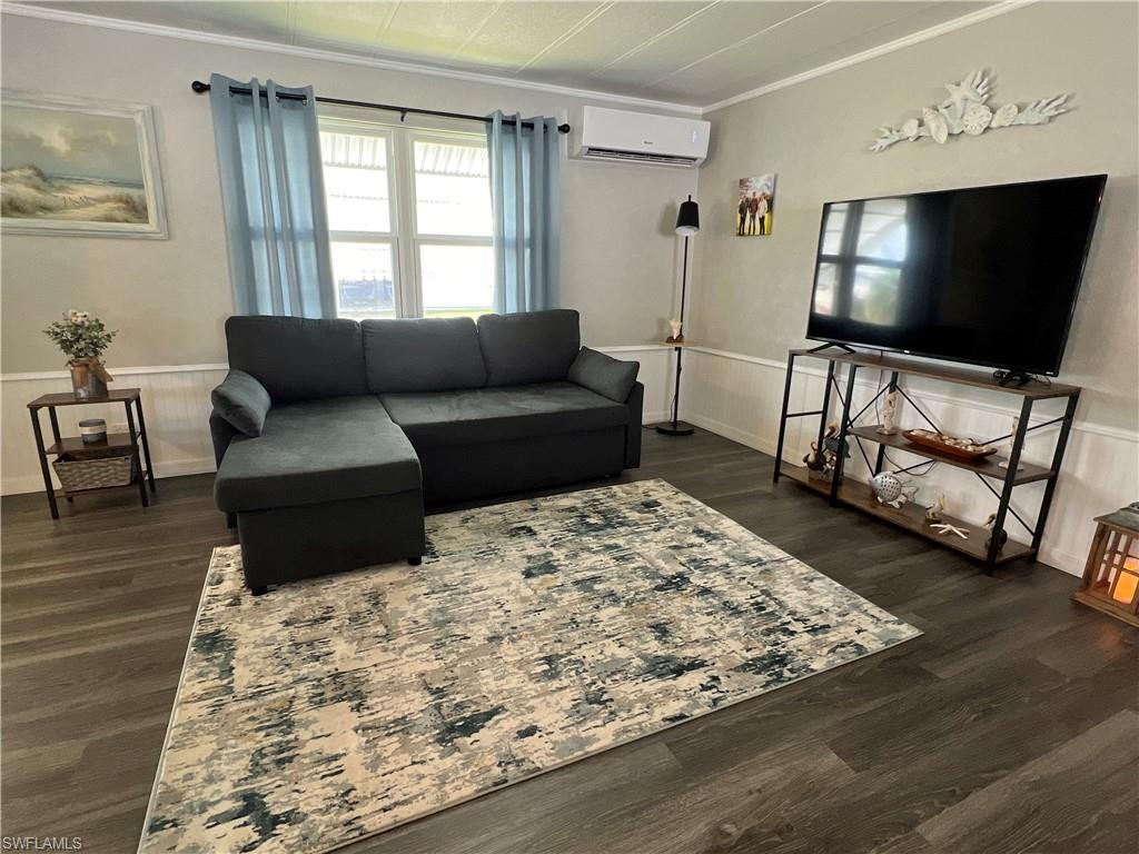 Living area featuring a wainscoted wall, dark wood-type vinyl flooring, and a wall mounted air/heat pump.