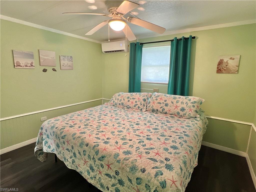 2nd Bedroom with ornamental molding, dark wood-type vinyl flooring, a wall mounted air/heat pump, ceiling fan, and a wainscoted wall