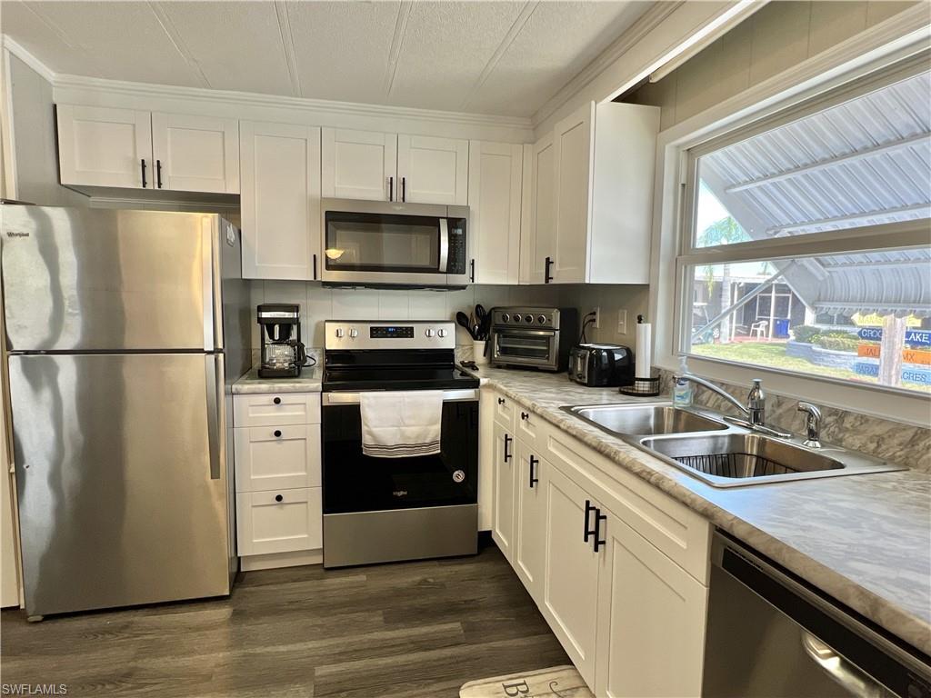 Kitchen featuring stainless steel appliances, white cabinets, light countertops, and dark wood-style vinyl floors