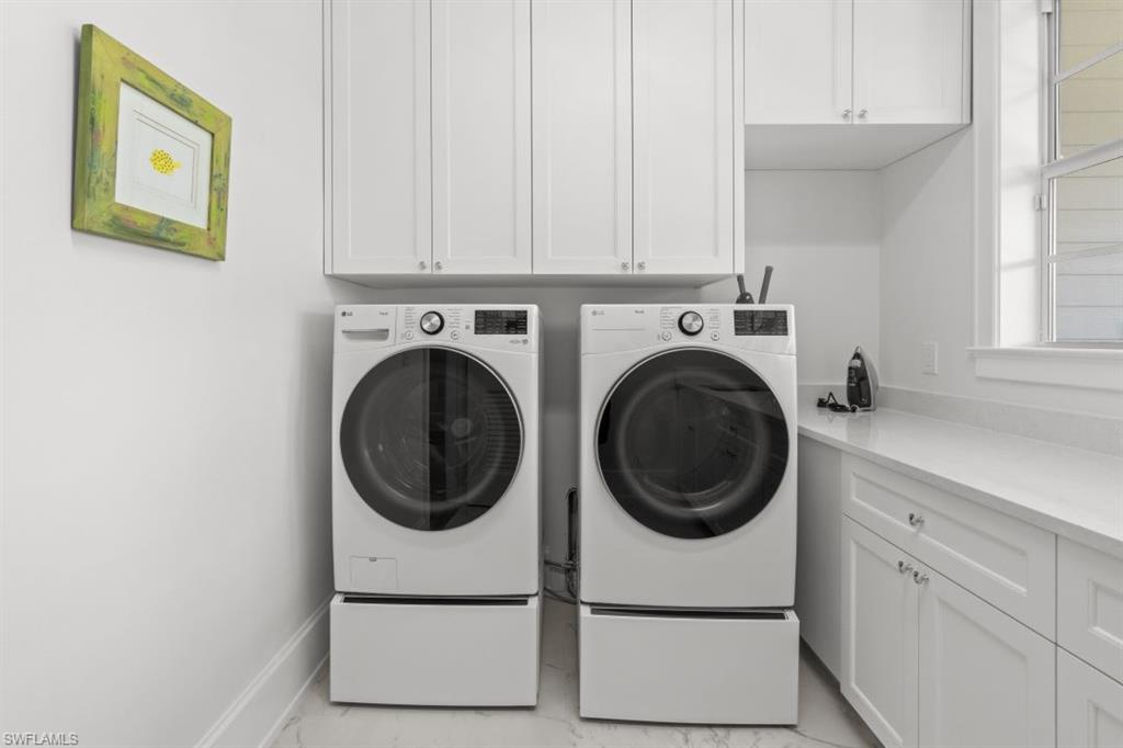 Laundry area featuring independent washer and dryer, cabinet space, and light marble finish flooring