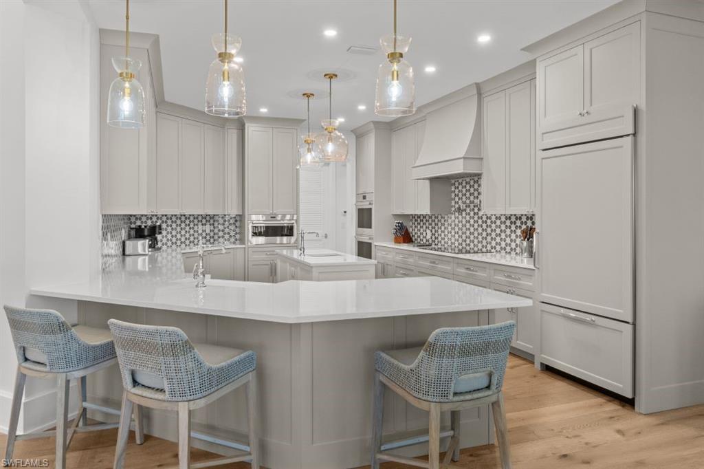 Kitchen featuring a peninsula, a breakfast bar area, light stone countertops, hanging light fixtures, and recessed lighting