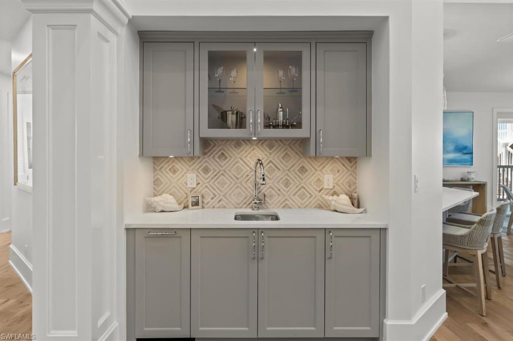 Indoor wet bar with gray cabinetry, light wood-style flooring, and backsplash