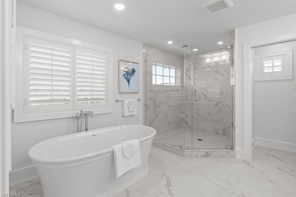 Bathroom featuring light marble finish floors, a freestanding bath, a marble finish shower, and recessed lighting