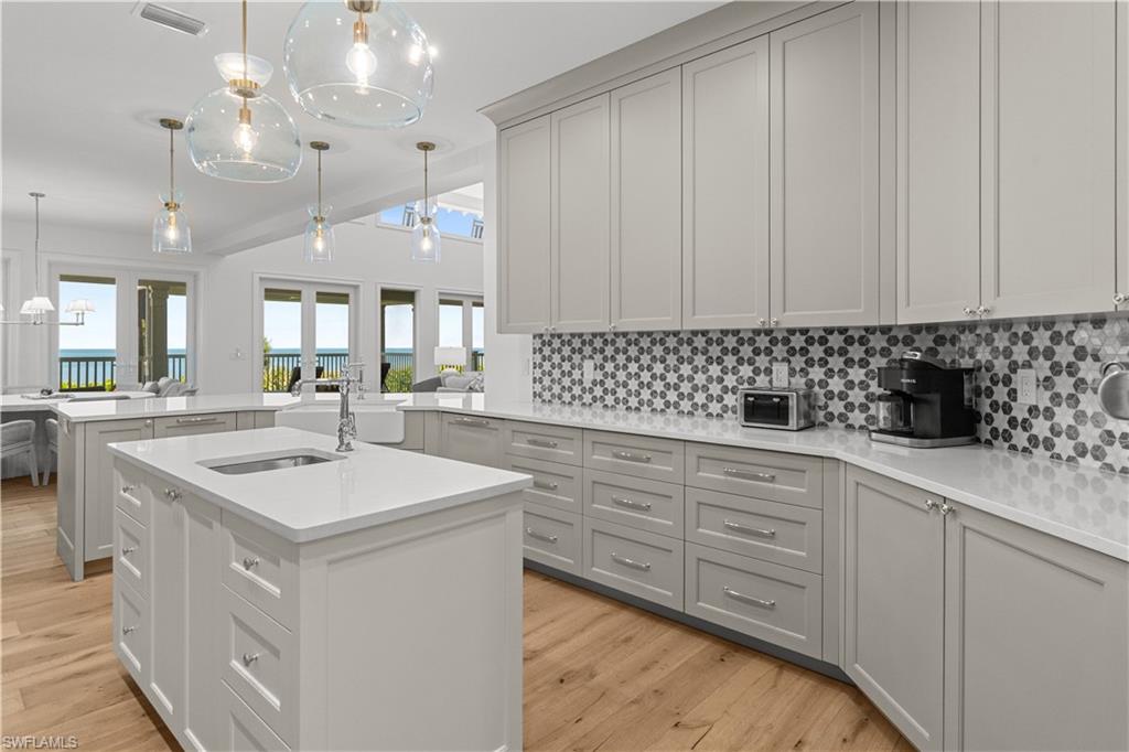 Kitchen with decorative light fixtures, backsplash, a peninsula, light stone countertops, and light wood finished floors
