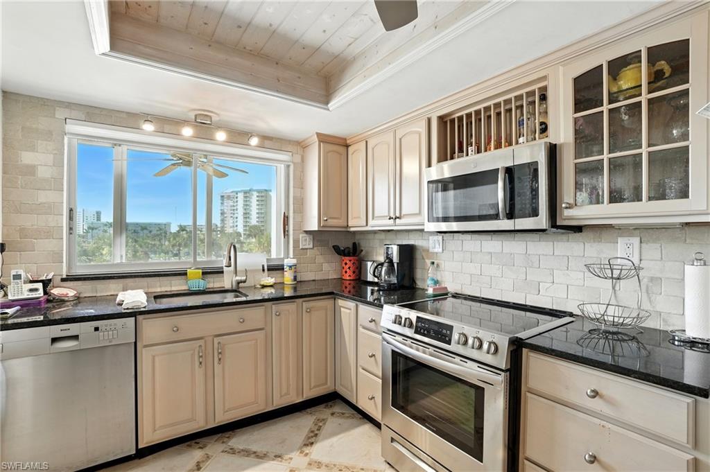 Kitchen with appliances with stainless steel finishes, a ceiling fan, dark stone counters, and inlaid floor details - Virtually Edited Image