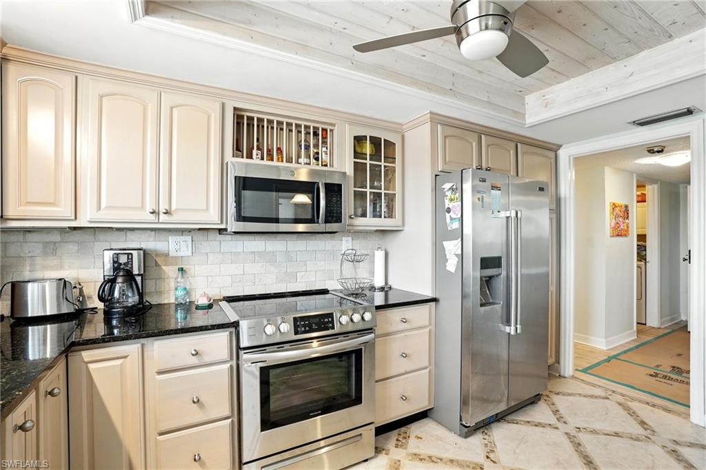 Kitchen with appliances with stainless steel finishes, inlaid floor details, backsplash, dark stone countertops, and a ceiling fan - Virtually Edited Image