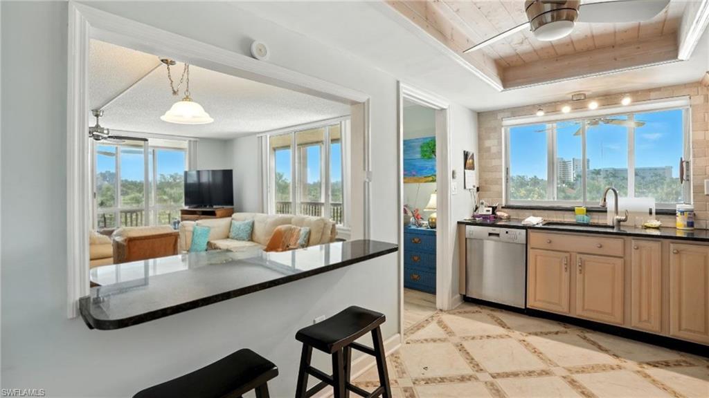 Kitchen featuring ceiling fan, dishwasher, a breakfast bar area, hanging light fixtures, and open floor plan - Virtually Edited Image