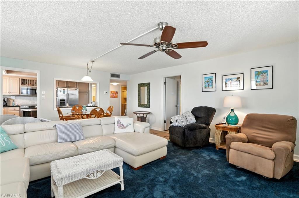 Living area with a textured ceiling, dark colored carpet, and ceiling fan - Virtually Edited Image