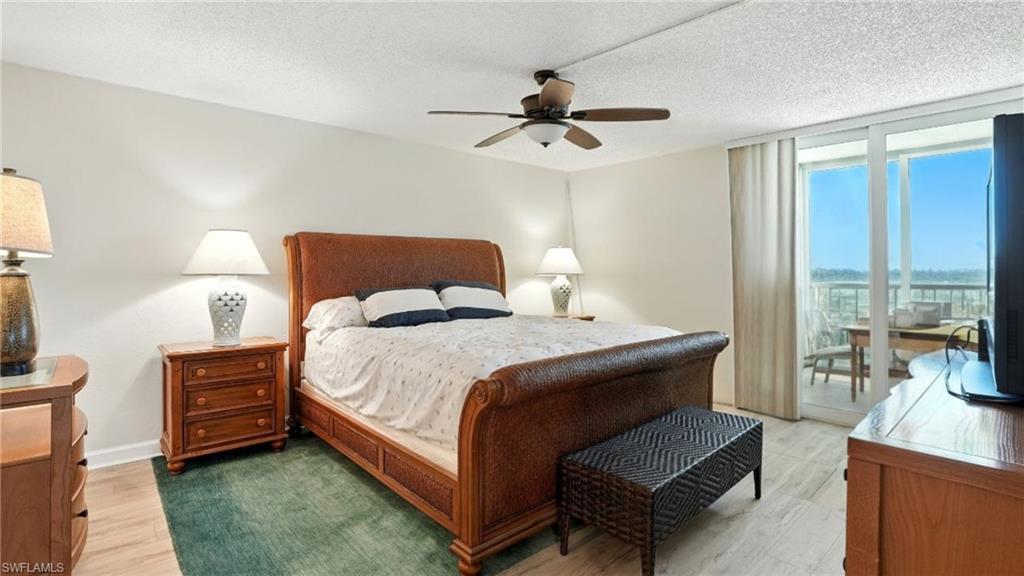Bedroom featuring access to exterior, light wood-style flooring, expansive windows, a textured ceiling, and a ceiling fan - Virtually Edited Image