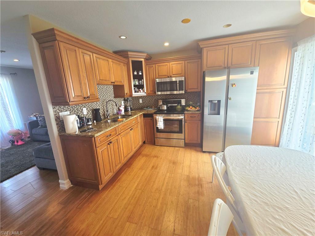 Kitchen with appliances with stainless steel finishes, dark stone countertops, light wood finished floors, brown cabinets, and recessed lighting